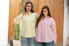 Two women wearing light-colored shirts outdoors with a blurred background